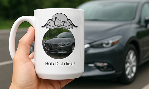 White mug with angel graphic and Mazda car, labeled “Hab Dich lieb!” — held in front of parked car