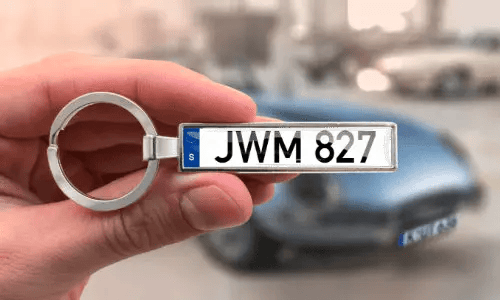 Sleutelhanger met aangepaste kentekenplaat, vastgehouden in de hand met auto op de achtergrond