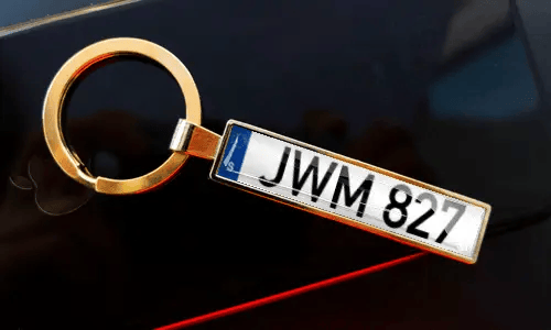 License plate keychain attached to keys in pocket with car in background