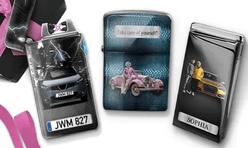Drei Metallfeuerzeuge mit personalisierten Designs. Das linke Feuerzeug zeigt eine Stadtsilhouette und ein Paar neben einem Auto mit der Aufschrift „BESTE OMA DER WELT“. Das mittlere Feuerzeug stellt ein rosafarbenes Oldtimer-Auto dar, darüber steht „HAB DICH LIEB OMA“. Das rechte Feuerzeug zeigt ein blaues Auto und ein Kennzeichen. Rosafarbene Schleifen verleihen dem Ganzen einen Geschenkcharakter.