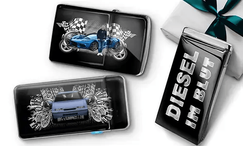 Two sleek black lighters featuring car themes, one with a blue car and checkered flags, another with a red car and gears. A third lighter reads 'DIESEL IM BLUT'. Gift-wrapped in the background.