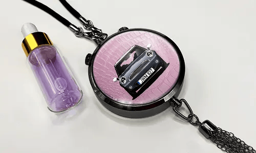 Pendant with pink background and white sports car, next to purple dropper bottle with gold cap