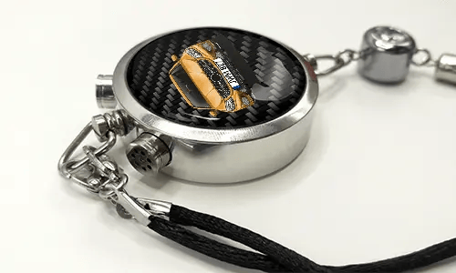 Round car key fob with carbon fiber face, buttons labeled LOCK and UNLOCK, braided black cord attached