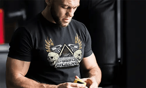 Schwarzes T-Shirt mit Grafik von Auto, Schädeln, Pistolen, goldenen Flügeln und sternförmigem Dreieckshintergrund